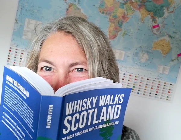Woman reading book with the title Whisky Walks Scotland. Map in background.