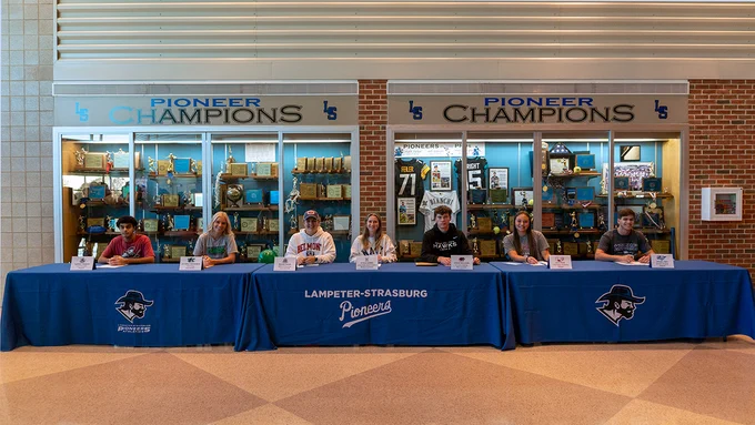 Seven people sitting at a table preparing to sign NLI, commitment letters