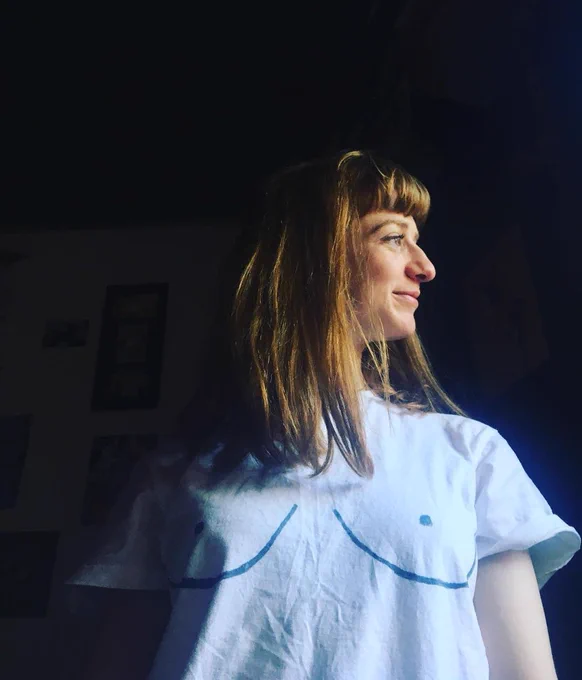 Side profile of a woman with short ginger hair, wearing a white t-shirt with boobs drawn on