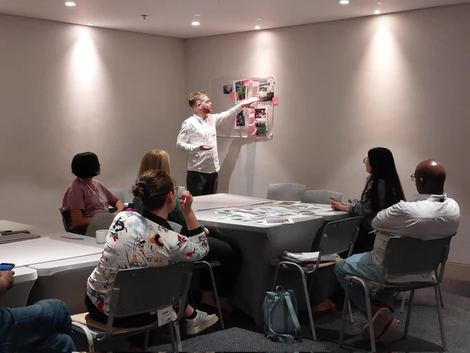 A group of people listen to a man explaining a  collage of photos featuring water.