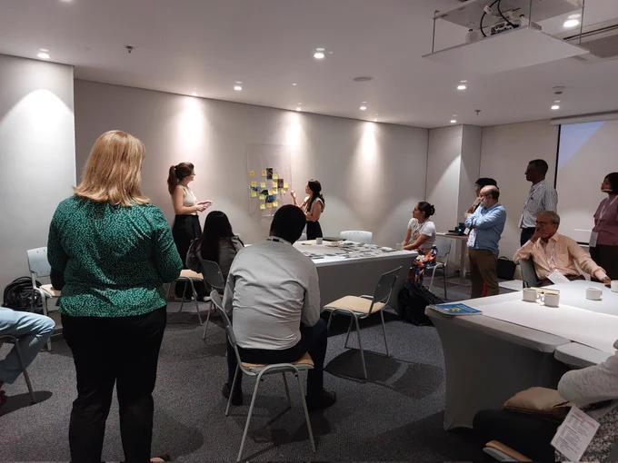 A group of people listen to a woman explaining a  collage of photos featuring water.