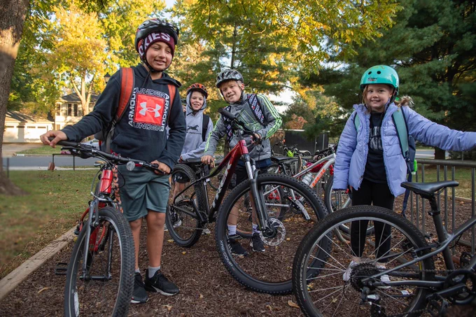 Four elementary-aged students are standing beside their bicycles. 