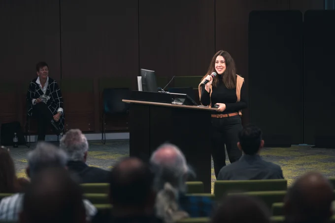 Woman on stage presenting with mic in hand. 