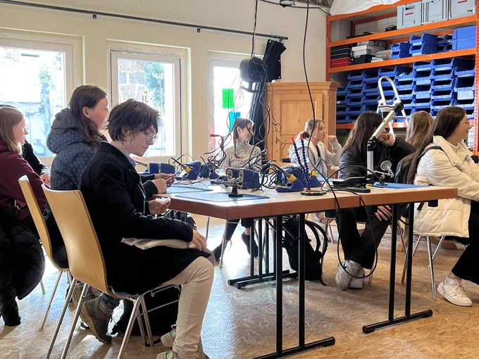 Schülerinnen sitzen um einen Tisch mit Lötstationen