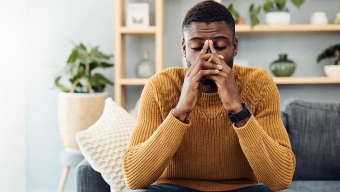 Man sitting on the couch with eyes closed experiencing tension or pain