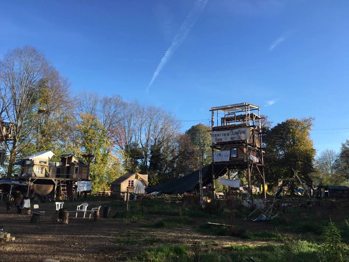 The same wooden tower can be seen from further away from another perspective. In the background you can see more trees, wooden huts and tree houses.