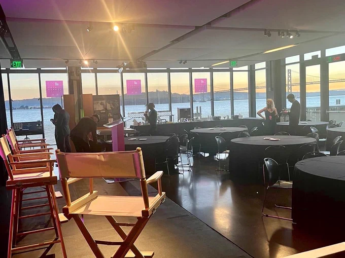a peaceful view of the Fisher Bay Observatory at sunrise. A few people are setting up for the day ahead and there’s a few director style chairs on the stage in the foreground.
