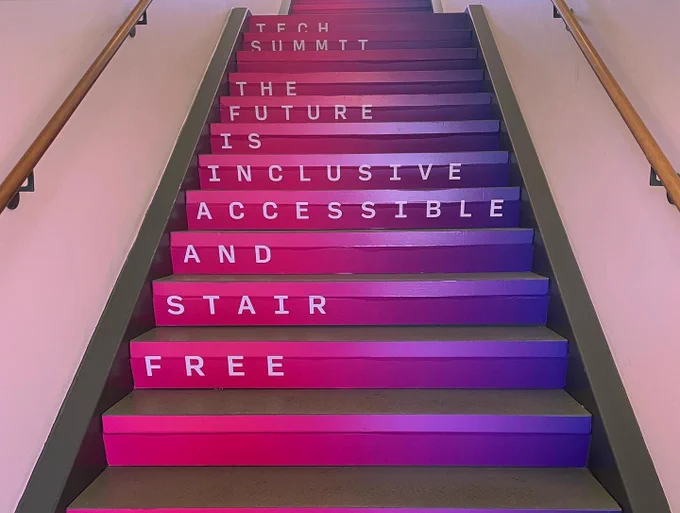 a narrow staircase with pink and purple laminate on the side wall of each step. In descending order, white text declares, “Tech Summit The Future Is Inclusive, Accessible and Stair Free.”