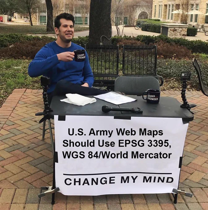A man sits behind a desk in a park. The sign on his desk says "U.S. Army Web Maps Should Use EPSG 3395, WGS 84/World Mercator" with "CHANGE MY MIND" written in all capital letters below.