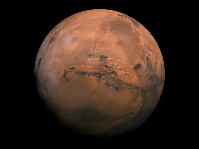 Mosaic image made from 102 NASA Viking Orbiter photos shows the full globe of Mars against a black background. Visible at the center of the rusty, reddish planet is Valles Marineris, an enormous canyon system around 1250 miles (~2000 kilometers) long, which stretches across most of the width of the planet in this view.