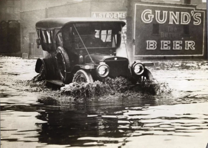 A car driving through floodwaters on W. 3rd St. in downtown Cleveland. A "Gund's Beer" sign is visible on the side of a building. (Source: Cleveland Public Library Photograph Collection)