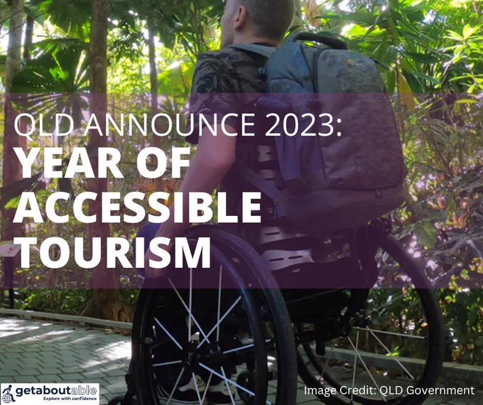 A person in a wheelchair travelling along a rainforest boardwalk. Text reads “QLD announce 2023 Year of Accessible Tourism”