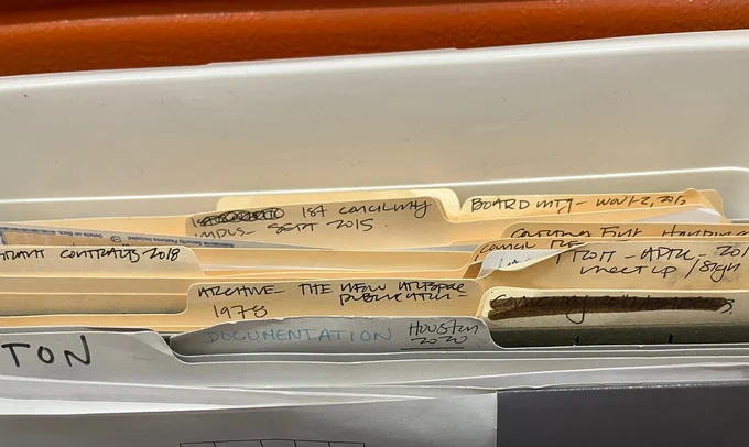 A closeup image of a set of Common Field’s manila file folders, arranged within dark olive divider folders inside of a white box. The folders are filled with papers, and are labeled with handwritten text indicating contents including “1st Council Meeting - Sept 2015,” “First Board Meeting…”, and “Documentation Houston 2020.” These folders comprise a portion of the material affects joining the Los Angeles Contemporary Archive’s Common Field collection.