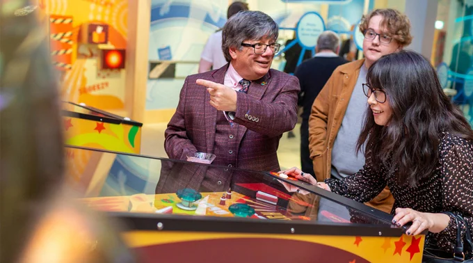 Three adults interacting with exhibit at Eureka! Science and Discovery. One is pointing at something. 