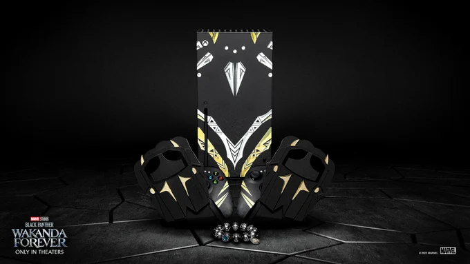Image of a custom designed Xbox Series X Console with Marvel Studios’ Black Panther: Wakanda Forever inspired artwork, two custom designed Controllers with Marvel Studios’ Black Panther: Wakanda Forever inspired artwork, two custom Designed Controller Holders with Marvel Studios’ Black Panther: Wakanda Forever inspired artwork, and a Custom Designed Kimoyo Beaded Bracelet. The artwork features a black, white and gold theme and the bracelet is black with blue bead accents. Text in the bottom left corner reads, " Marvel Studios’ Black Panther: Wakanda Forever: Only in theaters"