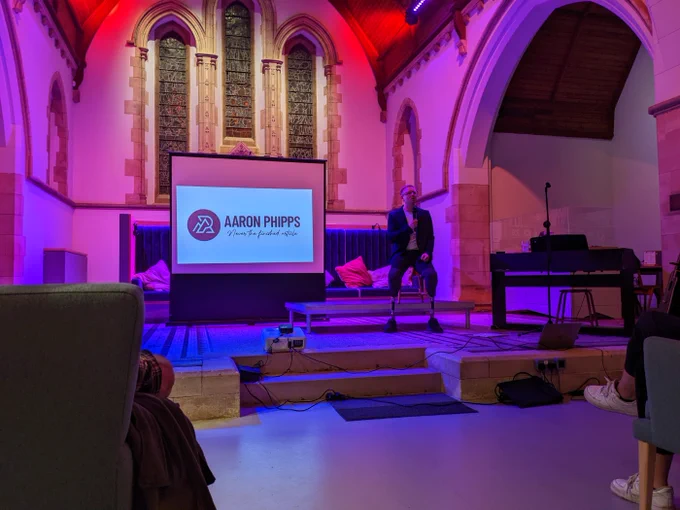 Aaron Phipps giving a talk in a colourful lit chapel