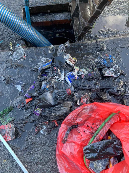 Gully wagon clearing a drain, with piles of drinks cans and bottles being pulled out and put in a red bag by Councilor Jackie Floyd