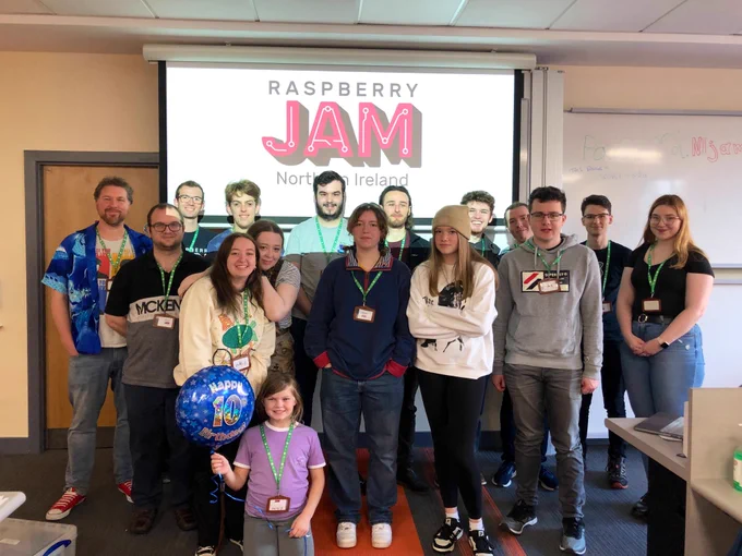 The Northern Ireland Raspberry Jam team standing together, with one holding a Happy 10th Birthday balloon.
16 people standing in the photograph with NI Raspberry Jam logo in behind.