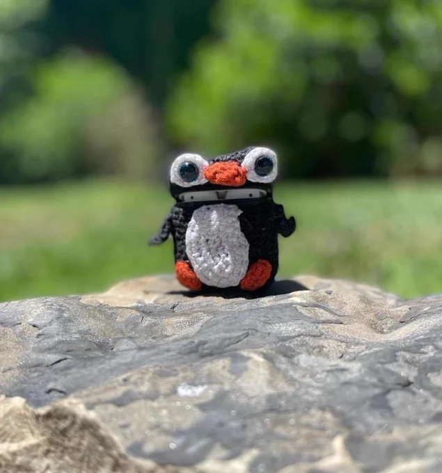 [image 3] crochet penguin headphone case sitting on top of a rock. 
