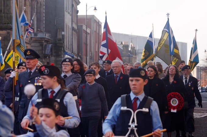 People walking in the Remembrance Sunday parade with flags from the Scouts behind