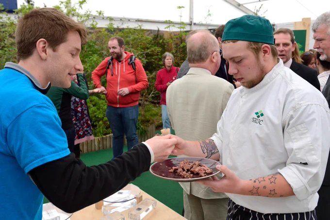 Two men share some samples of meat from a plate.