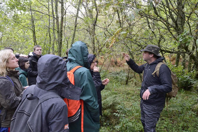 People in rain jackets listen to a tour guide as they forage for food in a forest.