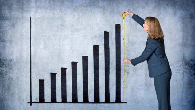 A bar chart with a women in a suit measuring the last bar.