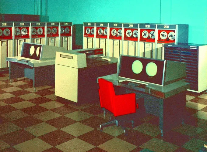 Bright red chair large tile floor and two monitors with double circle screens and tape readers in an L shape of the two far walls in this color enhanced marketing image that includes bright red, off white, gray, silver, and black hues.