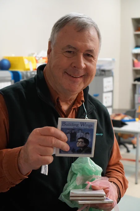 Don Johnston holding up a tile coaster with the cover of his book, Building Wings, pictured on the front. 