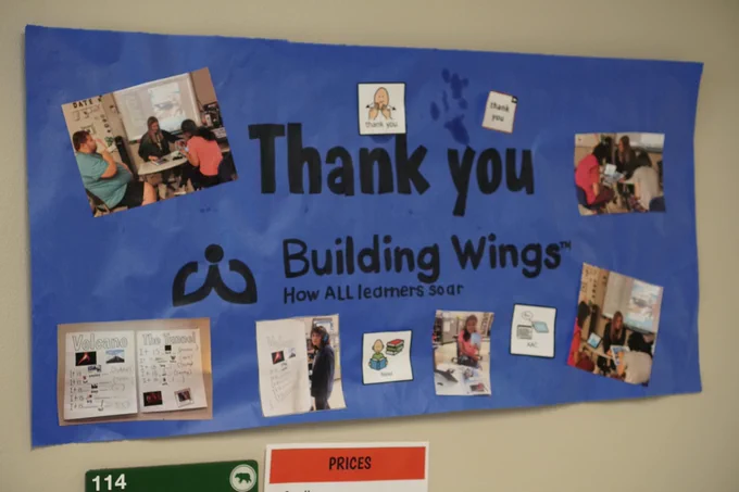 A blue poster that says Thank you Building Wings. Smaller text under Building Wings says "how ALL learners soar." There are pictures of students and examples of predictable charts they have been working on.
