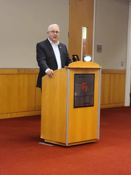 A man in a gray suit stands at a podium