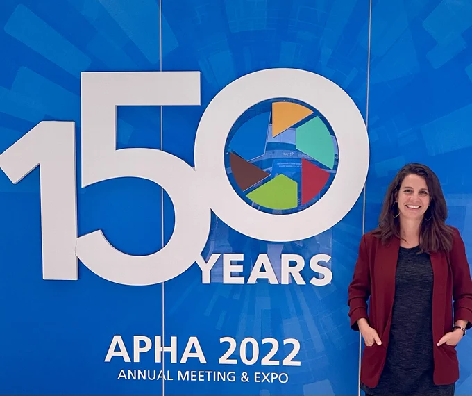 Dr. Paula Yuma stands next to the American Public Health Association logo at the 2022 meeting and expo.