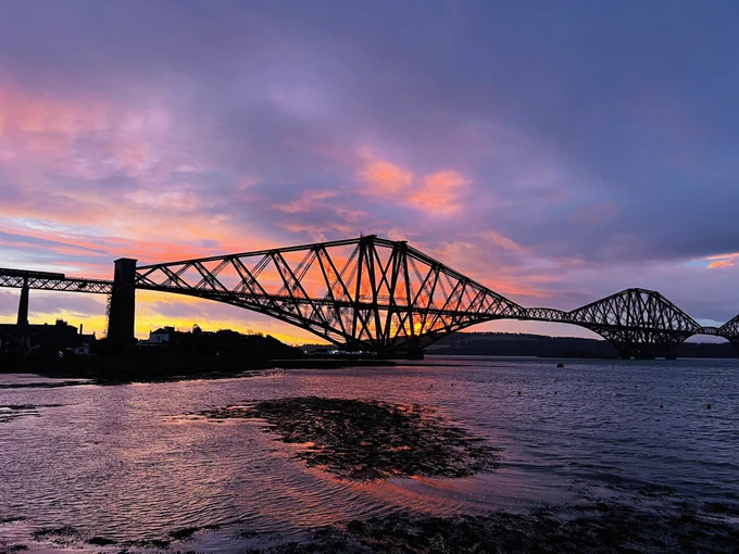 Forth rail bridge with a gorgeous orange and purple sunrise behind it.