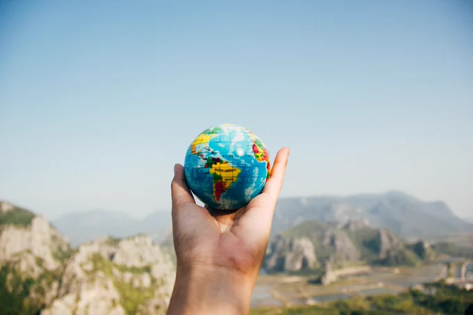 Person Holding World Globe Facing Mountain. Photo by Porapak Apichodilok