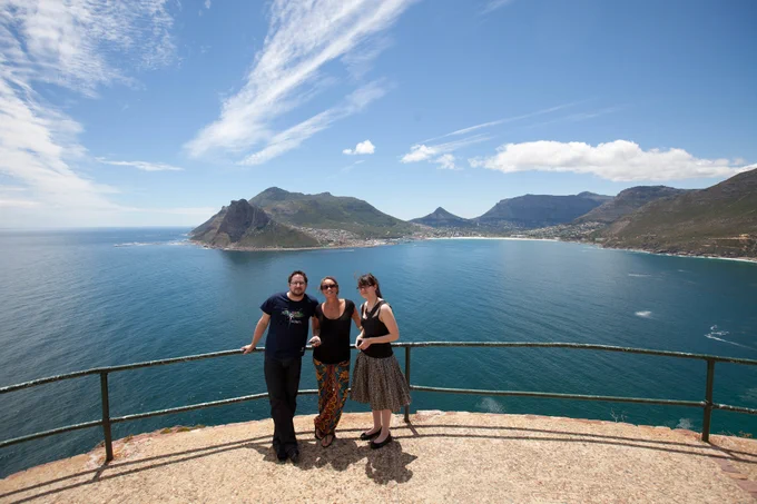 Matt, Caroline, and Ariel posing in front of a vast ocean and landscape in South Africa.