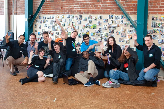 A dozen Science Hack Day ambassadors smiling and waving at the camera.