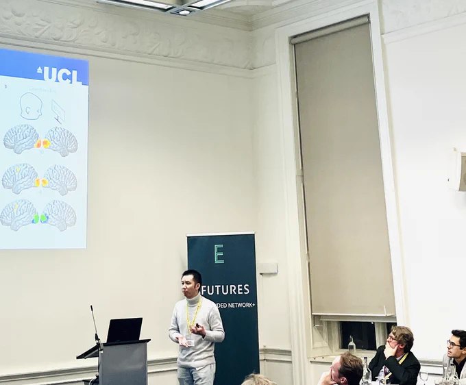 Photograph of Dr Hubin Zhao, an assistant professor at University College London, talking through a powerpoint presentation to a room of people