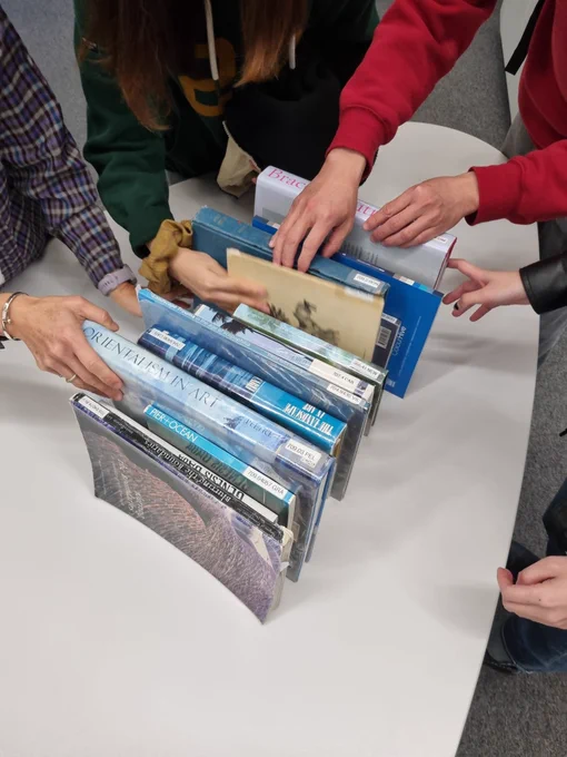 Lots of hands reaching for stacked books