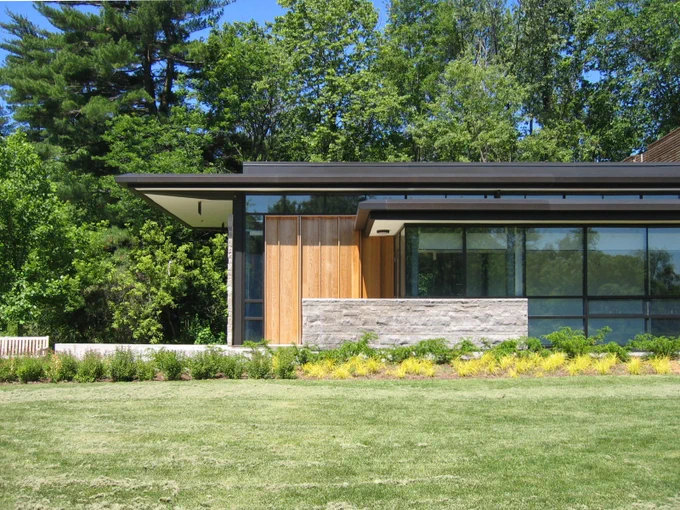 One storey building with large roof overhang, Large windows and large wooden panels.
