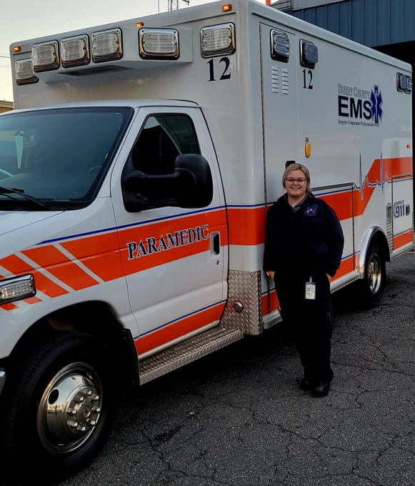A young woman stands next to an ambulance.