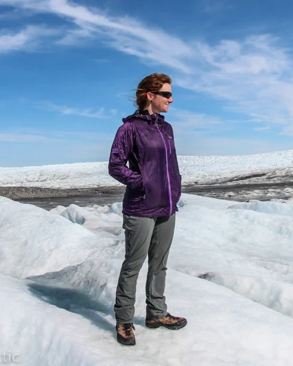 Marie, in purple jacket, grey trousers and hiking boots, stands on the Greenlandic Ice Sheet near Kangerlussuaq.