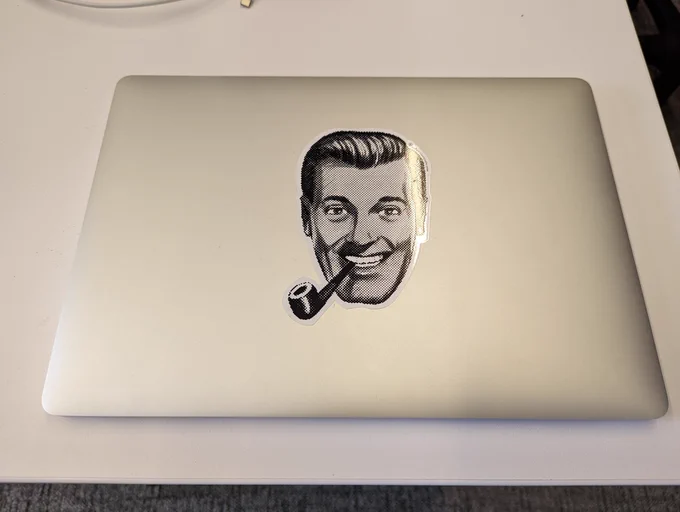 MacBook pro with a large sticker of JR "Bob" Dobbs on it.