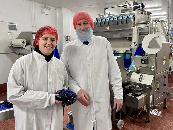 man and woman in white coats standing in a factory.