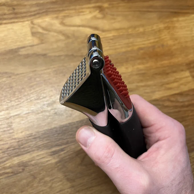 A solid looking metal garlic crusher with a black rubberised handle and a red plastic part to push the bits of garlic out of the holes. 