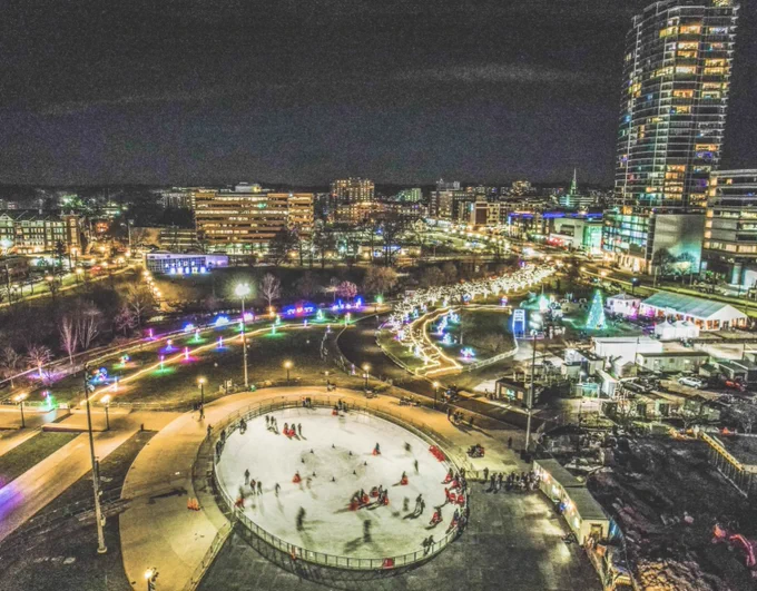 aerial shot of people skating on an ice rink at night with skyscrapers lit up around it
