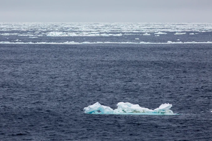 Photo from IODP Expedition 374. Photo shows a dark blue ocean with a field of sea ice in the distance. Caption: After several weeks of ice-free operations in the Ross Sea, Antarctica, winds from the east push a tongue of sea ice toward the vessel, forcing us to temporarily abandon Site U1524. Credit: William Crawford, IODP JRSO.