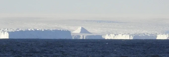 Photo from IODP Expedition 318. Photo is a panoramic view of the Antarctic coast with a dark blue ocean in the foreground and ice sheets in the background. Caption: View of the Antarctic coast from Site U1357. Credit Etiienne Claassen, IODP/TAMU.