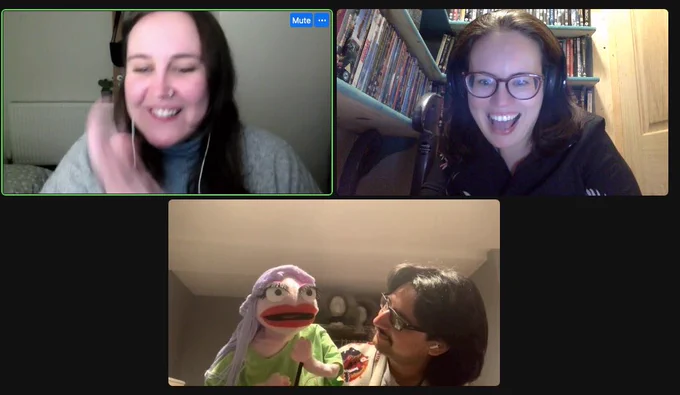 A screenshot of our zoom interview- Meg and Lexie look delighted at  their screens at J is showing them a puppet with purple hair.