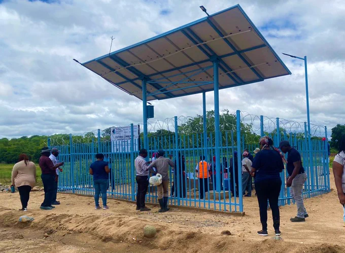 A group of people stand around a solar panel setup for a water scheme