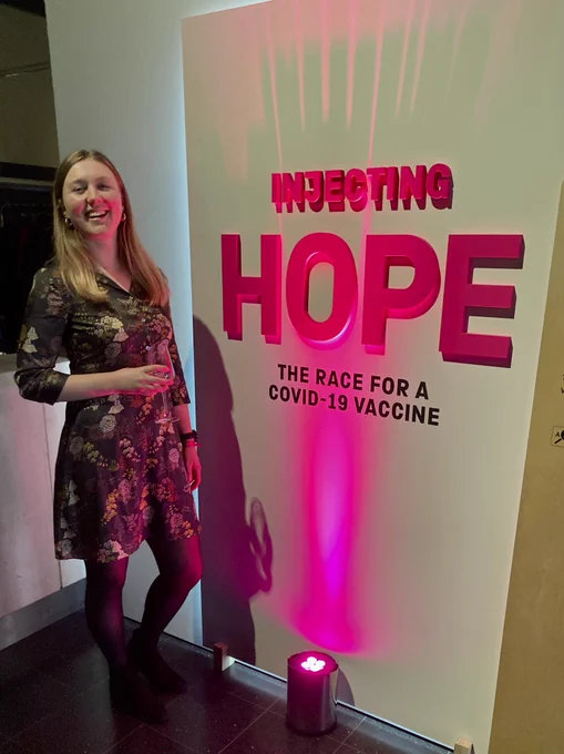 Woman smiling in front of exhibition title “Injecting Hope”